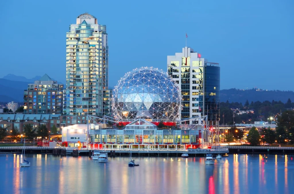 Skyline van Vancouver bij schemering met de verlichte koepel van Science World en wolkenkrabbers weerspiegeld in de haven