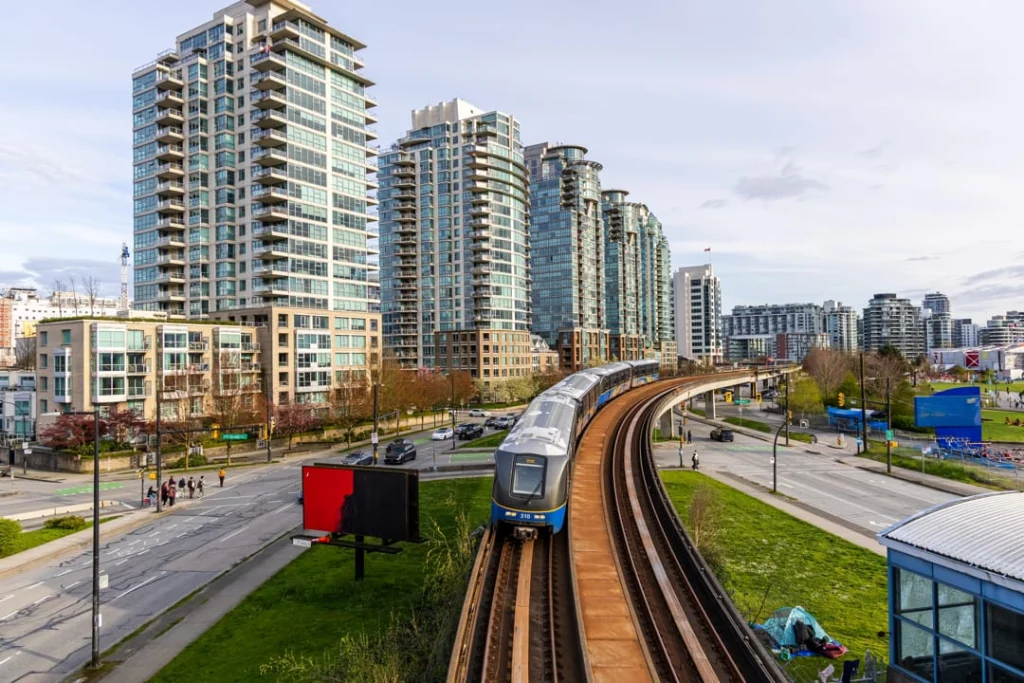 Een blauwe SkyTrein rijdt over een verhoogd spoor langs glazen woontorens en een brede straat in Vancouver