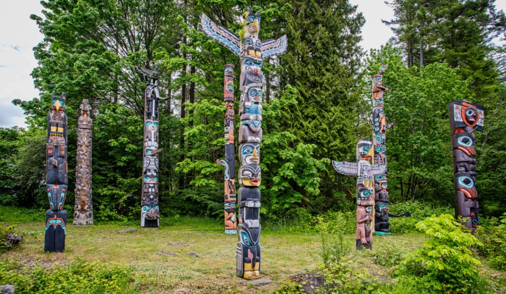 Een groep beschilderde houten totempalen staat tussen groene bomen in Stanley Park in Vancouver