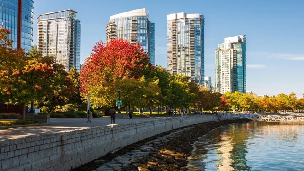 Wandelpad langs het water in Vancouver met kleurrijke herfstbomen en hoge glazen wolkenkrabbers op de achtergrond