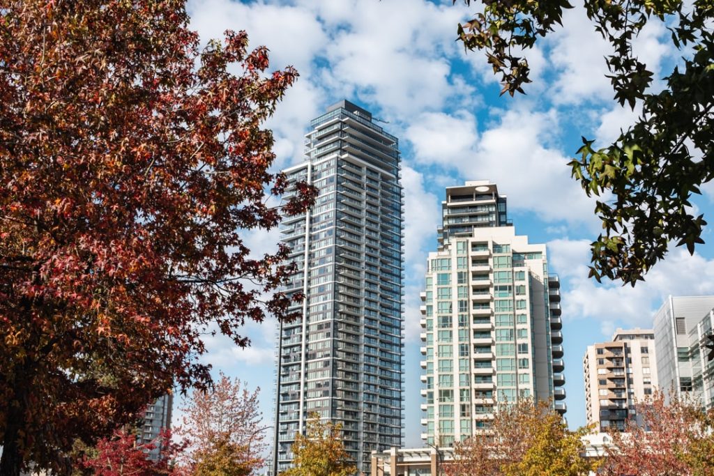 Hoge glazen appartementstorens gezien tussen bomen met rode en oranje herfstbladeren onder een blauwe lucht in Vancouver