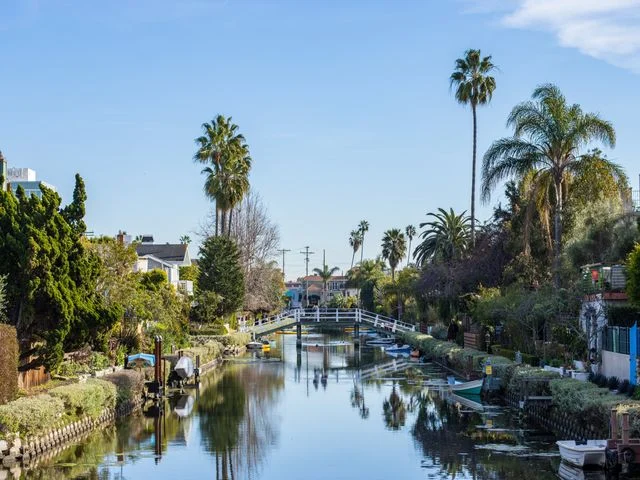 Rustig kanaal met een witte houten brug, bootjes en huizen tussen palmbomen in de Venice Canals