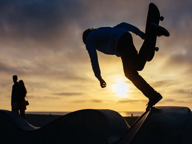 Silhouet van een skateboarder die een sprong maakt op een skatebaan tegen een oranje avondlucht bij Venice Beach