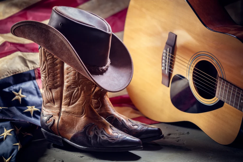 Bruine cowboyhoed en versierde cowboylaarzen naast een akoestische gitaar op een Amerikaanse vlag