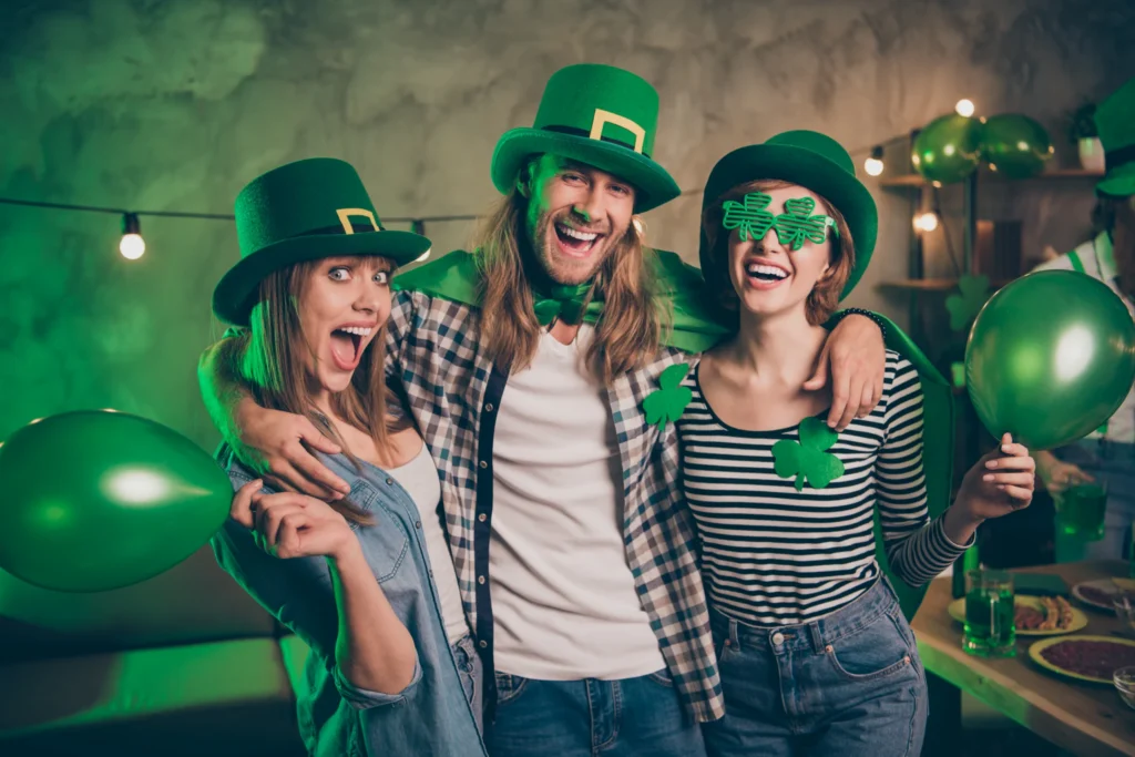 Drie lachende vrienden met groene hoeden bril en ballonnen vieren Saint Patrick's Day op een feestje