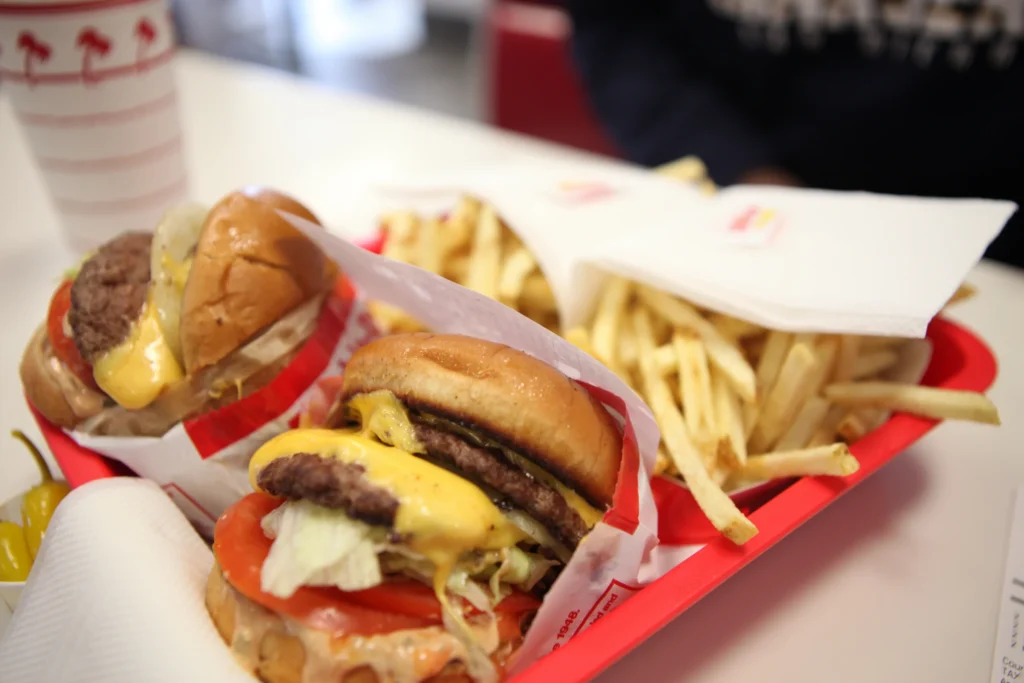 Twee dikke cheeseburgers met sla en tomaat naast een portie friet op een rood dienblad in een fastfoodrestaurant