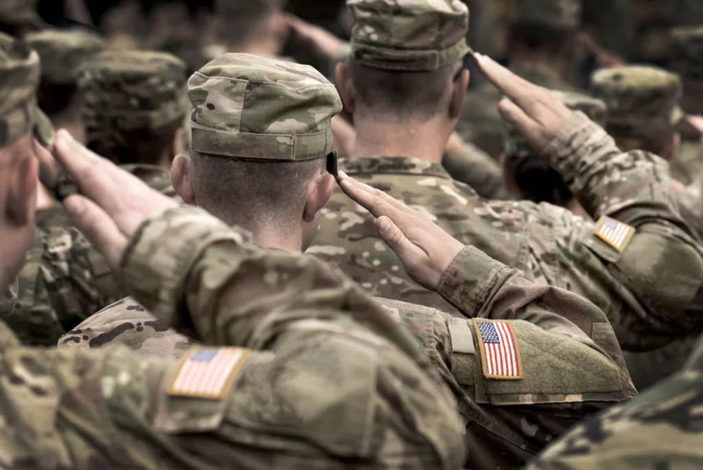 Groep militairen in camouflagepak met Amerikaanse vlagpatches op de mouw salueert gezien van achteren in close-up