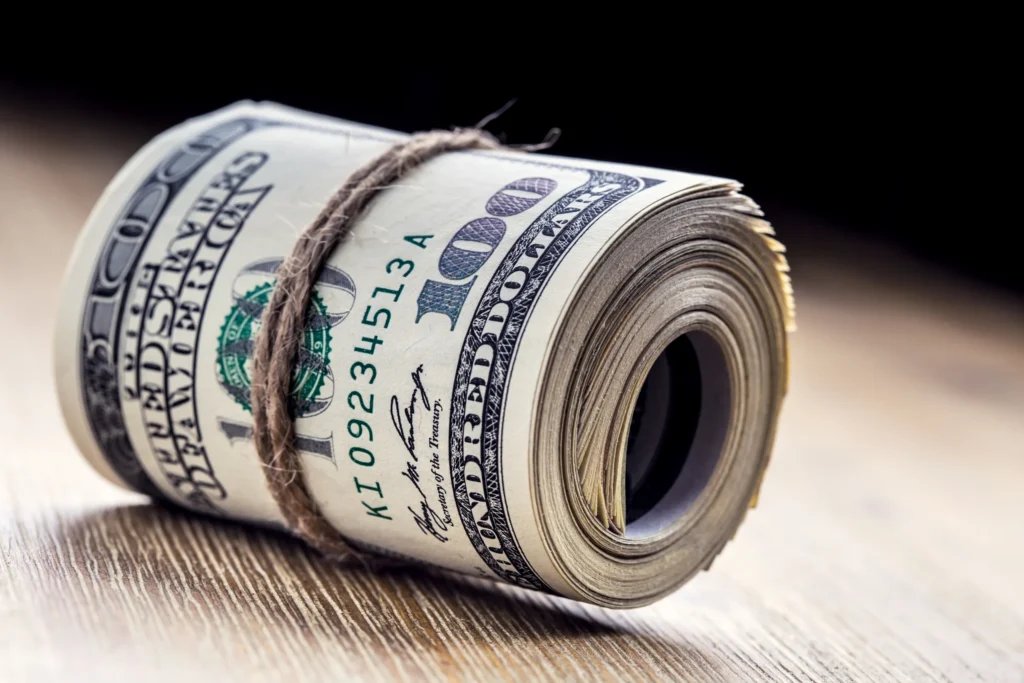 Close-up van een met touw samengebonden rol honderd dollarbiljetten op een houten ondergrond