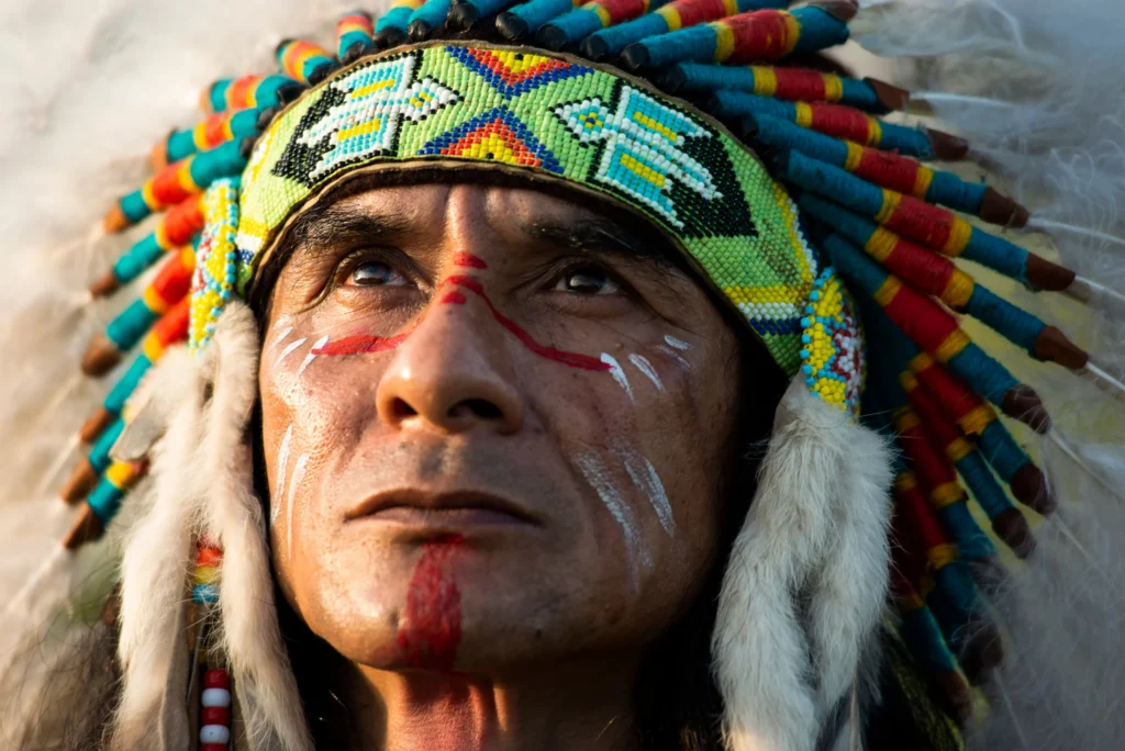 Close-up portret van een man met beschilderd gezicht en een kleurrijke veren hoofdtooi met kralenband