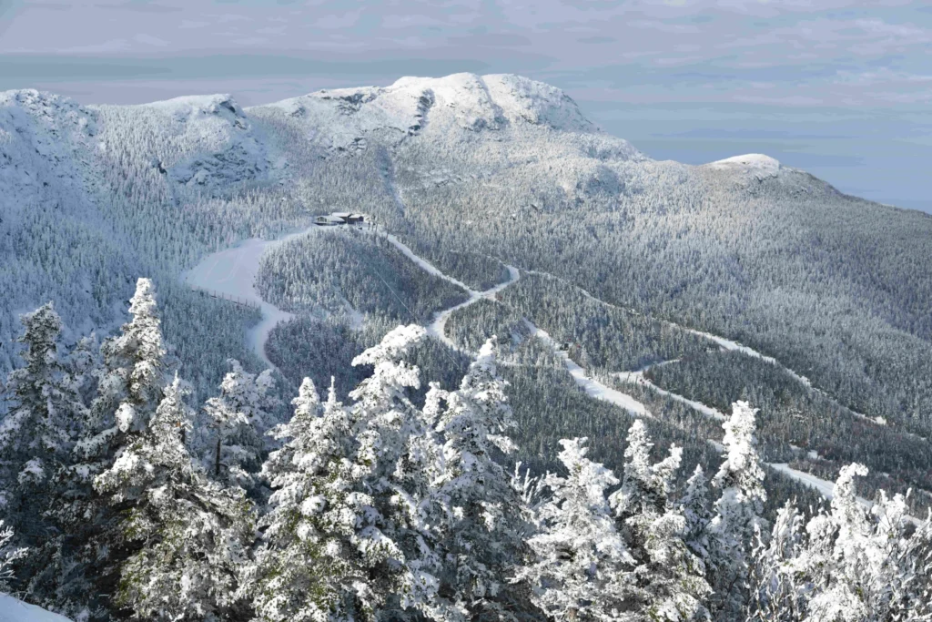 Uitzicht over besneeuwde dennenbossen en skipistes met een bergstation op de top in Vermont