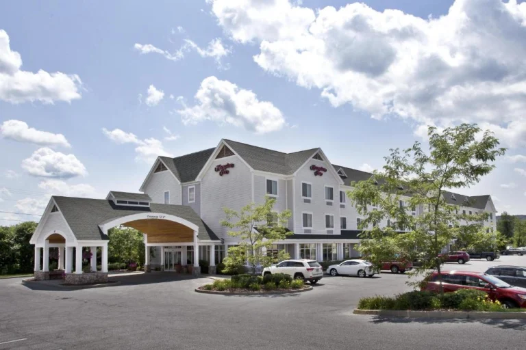 Wit hotelgebouw van Hampton Inn met een overdekte oprit en geparkeerde auto's onder een bewolkte lucht in Vermont