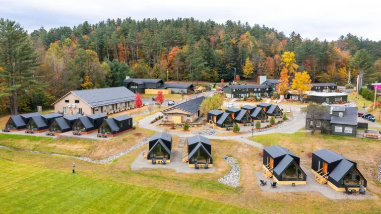 Luchtfoto van een vakantiepark met houten hoofdgebouwen en losstaande cabins tussen bomen in felle herfstkleuren in Vermont