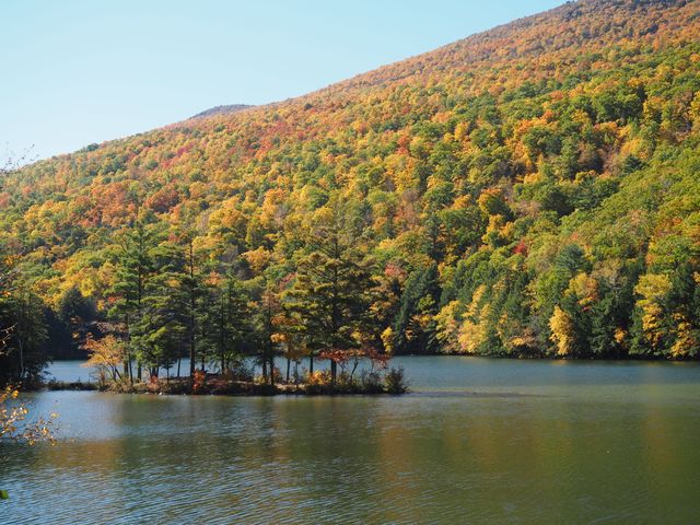 Rustig groen meer met een klein begroeid eilandje voor een berghelling vol bomen in felle herfstkleuren in Vermont