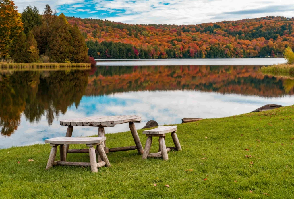 Een houten picknicktafel op een grasveld aan een rustig meer in Vermont, omringd door heuvels met felle herfstkleuren
