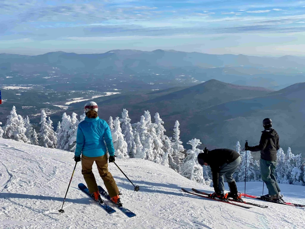 Drie skiërs staan op een besneeuwde piste in Vermont met uitzicht op besneeuwde bergen en dalen op de achtergrond