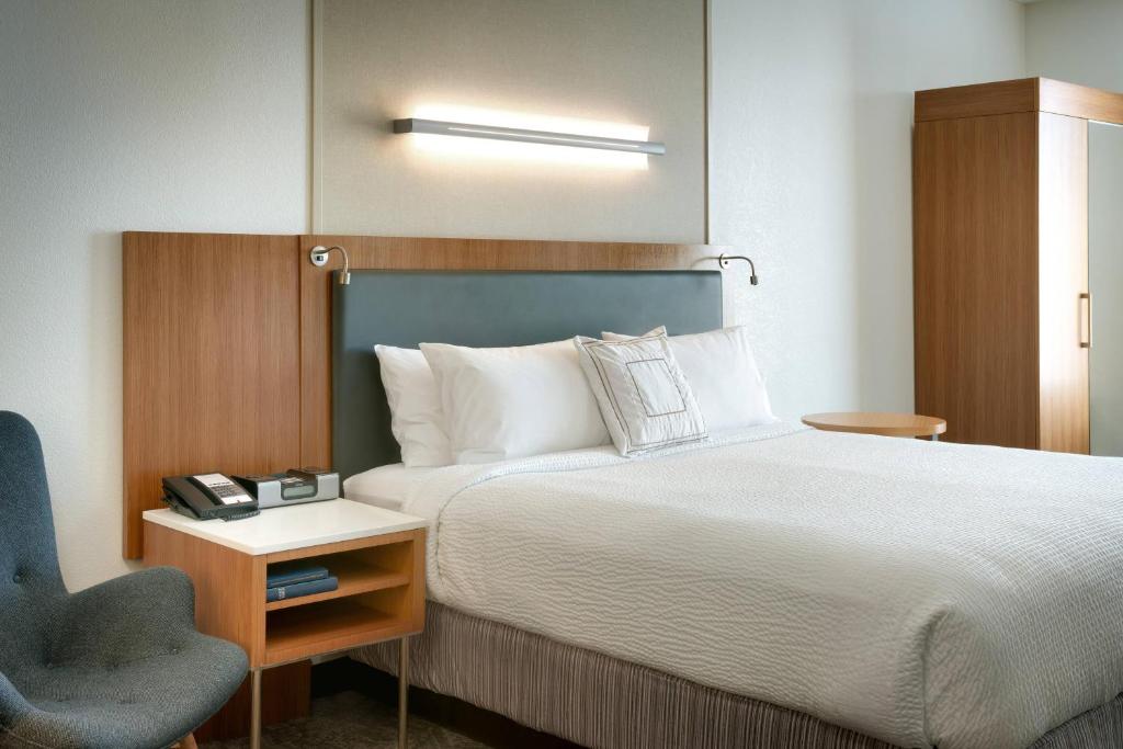 Hotelkamer met een bed met donker houten hoofdbord, een blauwe fauteuil en een kledingkast op de achtergrond