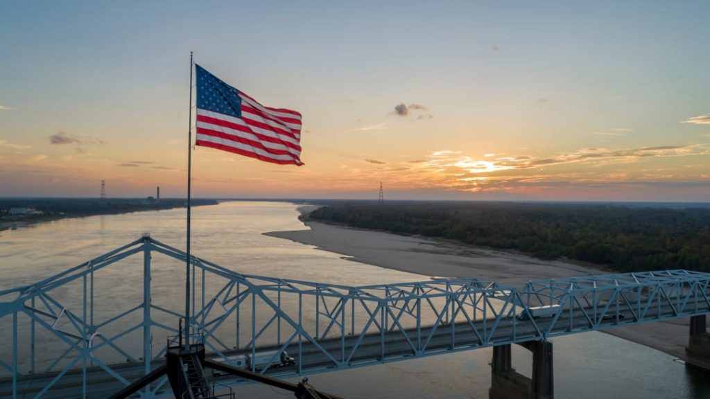 Grote Amerikaanse vlag op een brugpyloon met uitzicht over de brede Mississippi rivier bij zonsondergang nabij Vicksburg