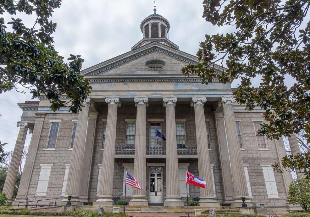 Grijs stenen gebouw met zuilengalerij, een koepeltje en de Amerikaanse en Mississippi vlag ervoor in Vicksburg