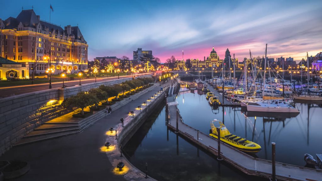 Jachthaven van Victoria bij avondschemering met verlichte historische gebouwen, waaronder het Empress Hotel, weerspiegeld in het water