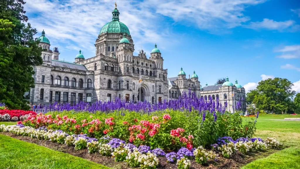 Het historische parlementsgebouw van Victoria met groene koepels en een uitbundig bloemenperk in paars, roze en wit ervoor
