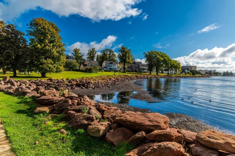 Groen park met rode rotsblokken aan een rustig meer, met huizen tussen de bomen in Victoria