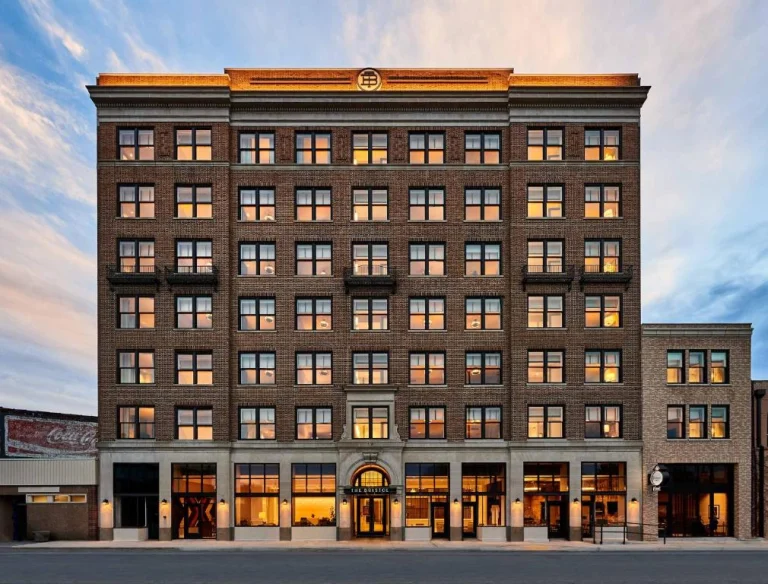 Een verlicht bakstenen hotelgebouw met meerdere verdiepingen en boogramen staat aan een straat in Virginia tijdens de schemering