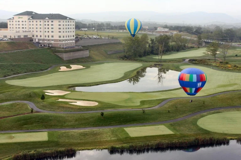 Twee kleurrijke heteluchtballonnen zweven boven een uitgestrekte golfbaan met waterpartijen en een groot hotel in Virginia