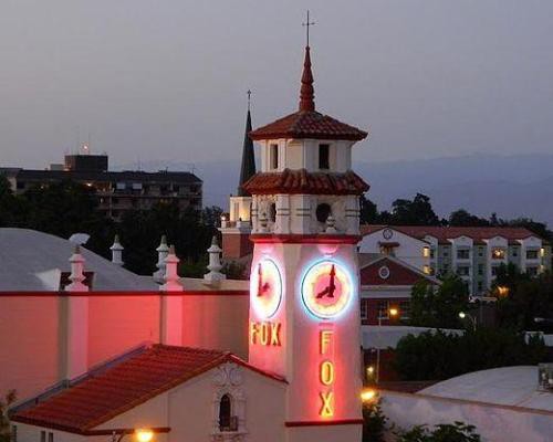 Verlichte Spaanse klokkentoren van het Fox Theatre met neonletters in Visalia tegen een blauwe avondlucht met gebouwen op de achtergrond