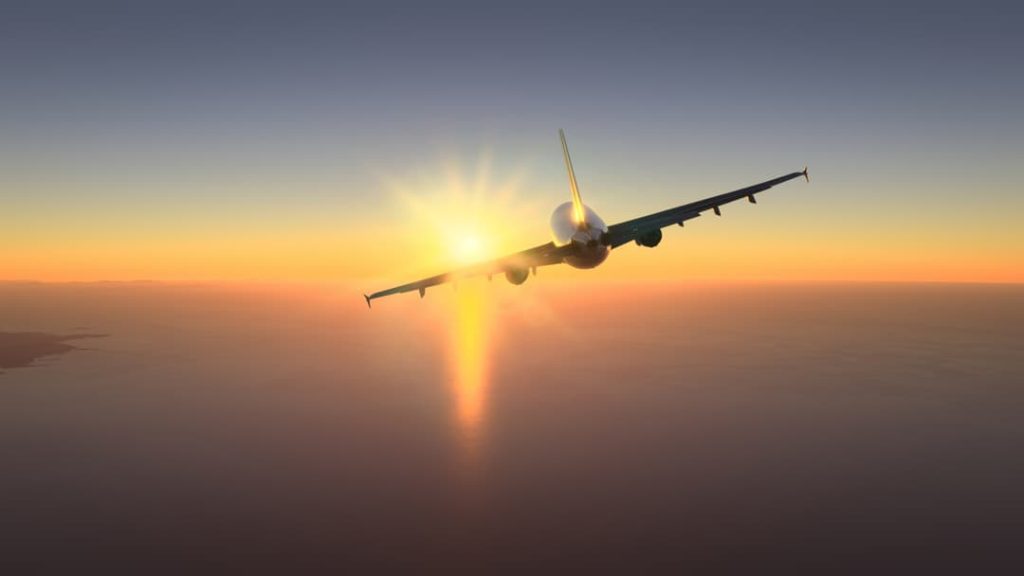 Silhouet van een vliegtuig dat recht op de ondergaande zon af vliegt boven een uitgestrekte oceaan met een kustlijn in de verte