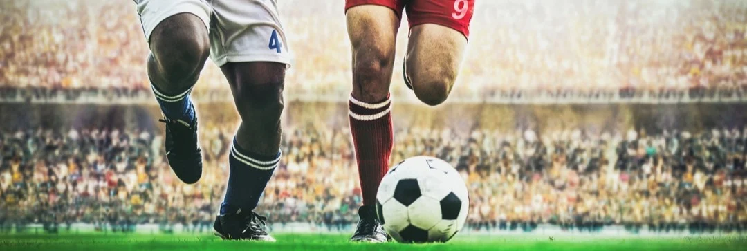 Close-up van de benen van twee voetballers in duel om de bal met een vol gejuich stadion op de achtergrond