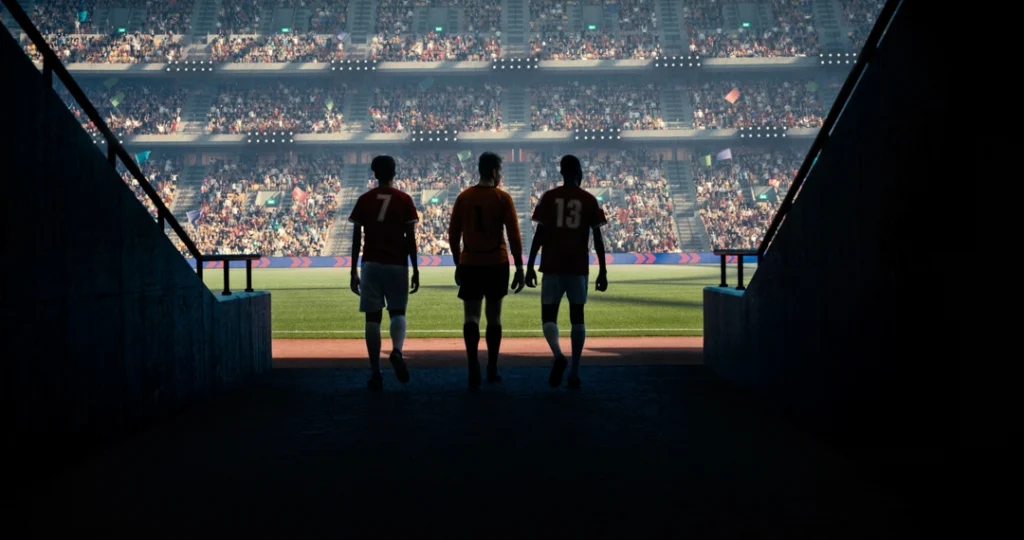 Silhouetten van drie voetballers lopen door een donkere tunnel het felverlichte veld met vol stadion op