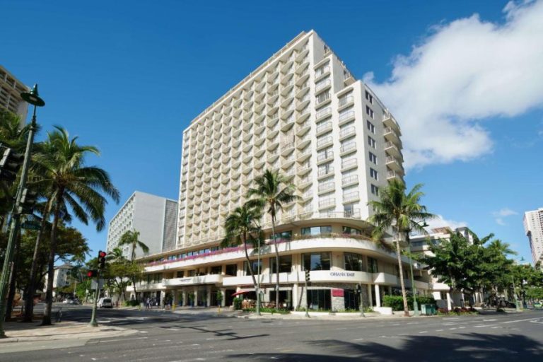 Wit hoog hotelgebouw met balkons op een straathoek met palmbomen en verkeerslichten in Waikiki