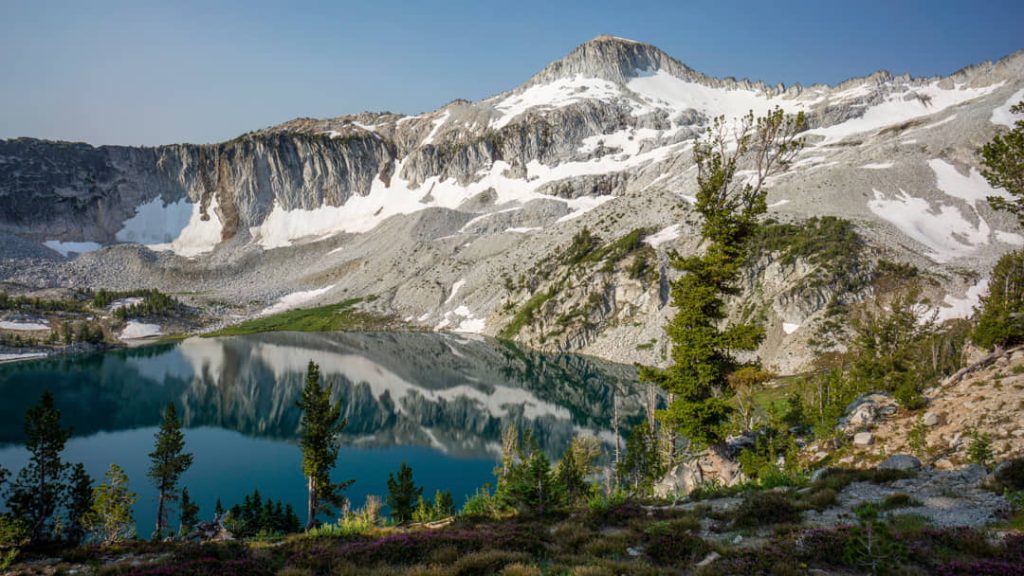 Helder turquoise meer omringd door rotsachtige besneeuwde bergen in het Wallowa gebergte met dennenbomen op de voorgrond