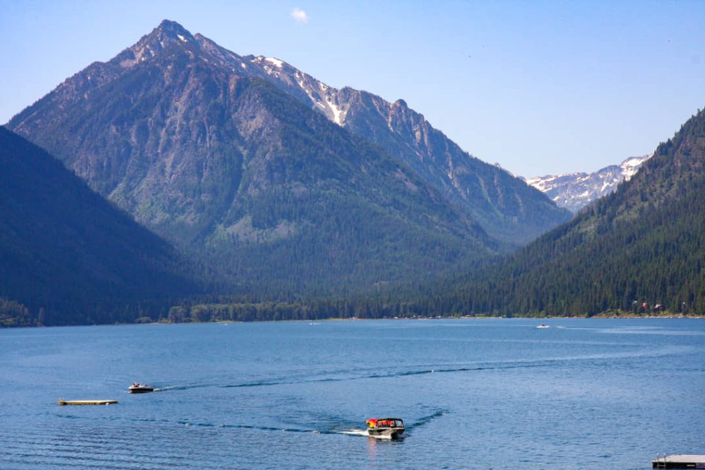 Twee boten varen over het rustige water van Wallowa Lake met steile beboste bergen op de achtergrond