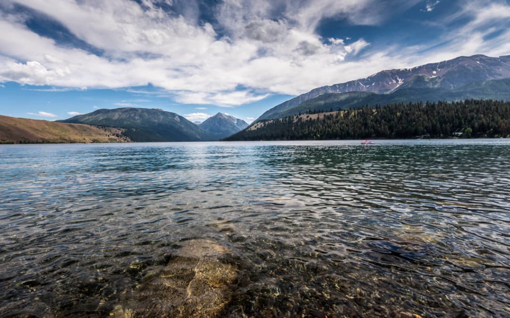 Kalm helder water van Wallowa Lake met op de achtergrond een bergketen deels bedekt met sneeuw onder een blauwe hemel