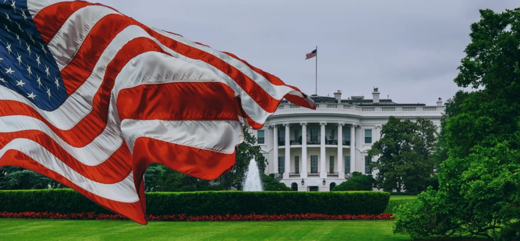 Grote wapperende Amerikaanse vlag op de voorgrond met het Witte Huis en een fontein op het gazon op de achtergrond