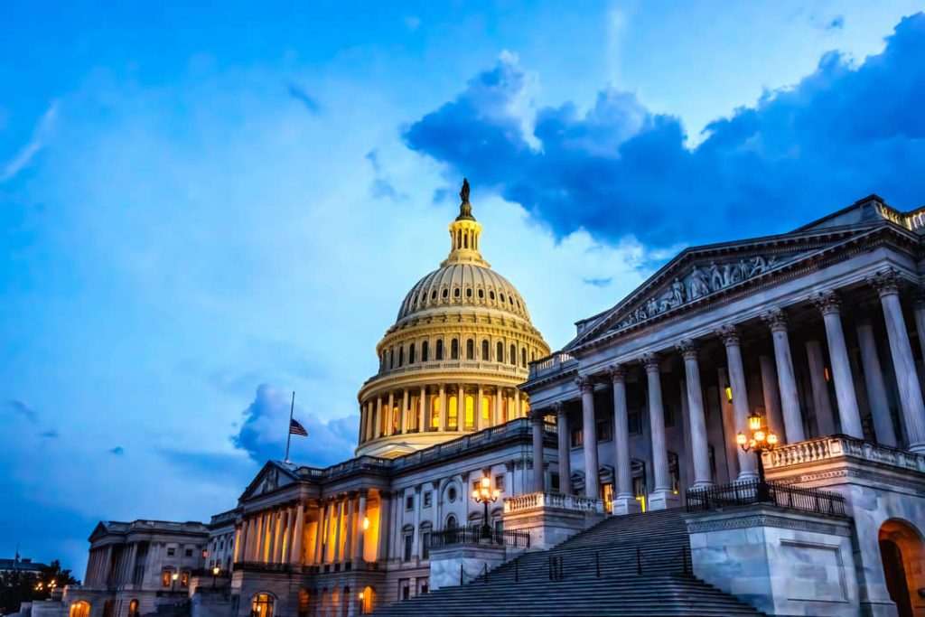 De verlichte koepel en zuilengalerij van het Capitool in Washington DC tegen een blauwe avondlucht met wolken