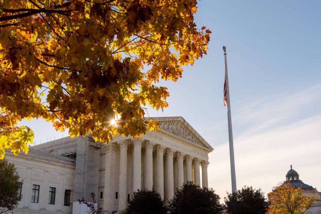 Zuilengalerij van het Hooggerechtshof in Washington DC met een halfstok hangende vlag en een boom met gele herfstbladeren op de voorgrond