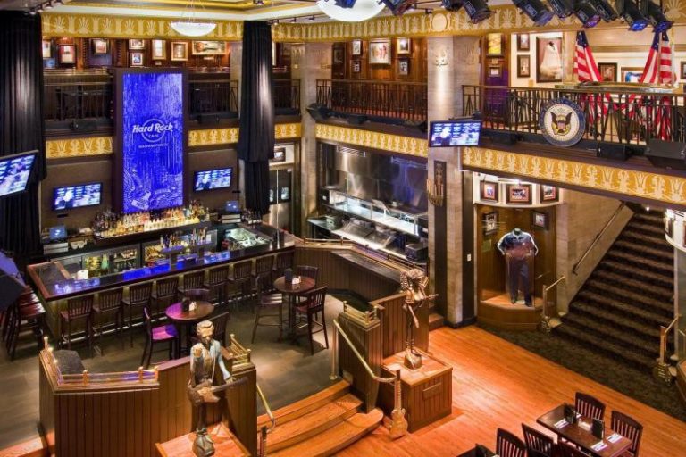 Sfeervol interieur van het Hard Rock Cafe met een grote bar, gitaren aan de muur en een verlicht logo op een scherm