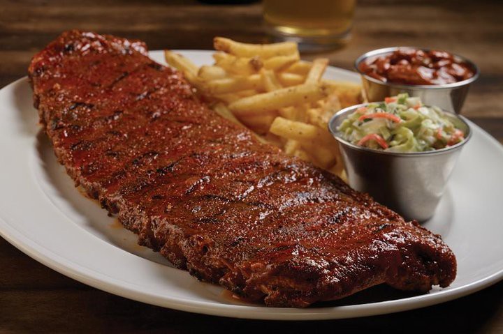 Geglaceerde spareribs met een dikke bbq-korst, geserveerd met een portie friet en twee blikjes met saus en koolsalade