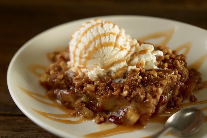 Bord met een warme fruitcrumble met noten, een bol vanille-ijs erop en een sliert karamelsaus