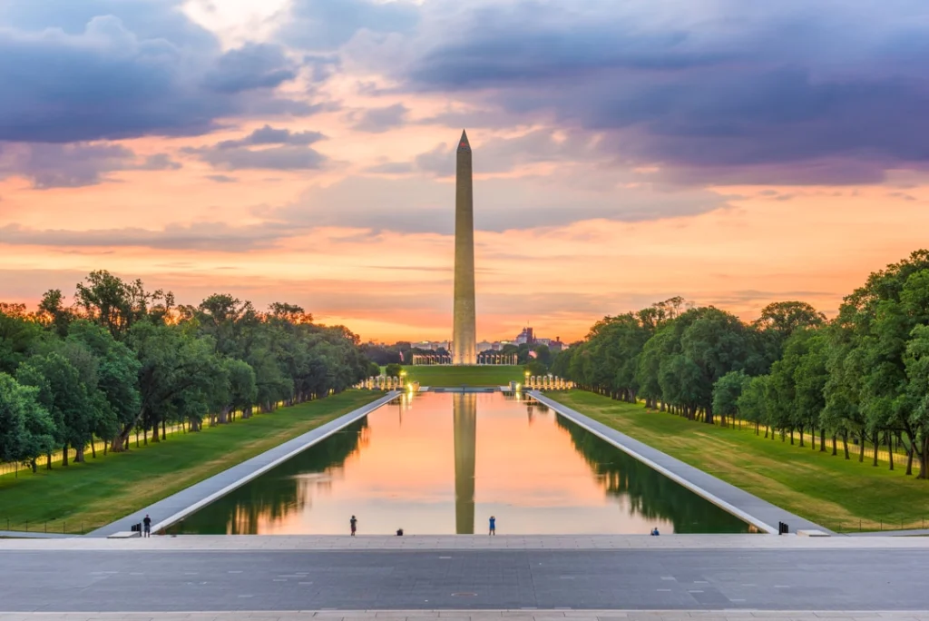 Het Washington Monument weerspiegeld in de reflecting pool met een oranje en paarse lucht bij zonsondergang in Washington DC