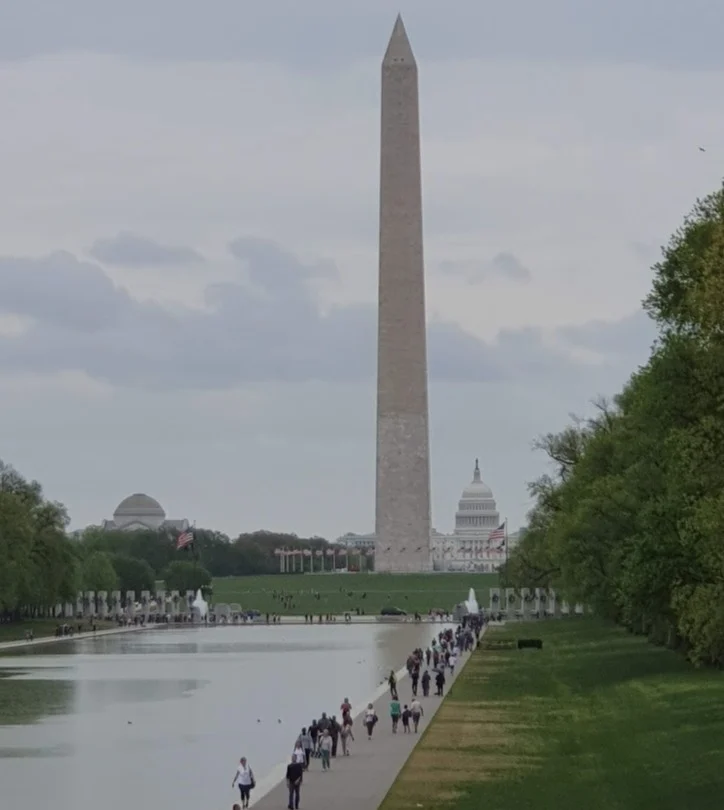 Bezoekers wandelen langs de Reflecting Pool naar het Washington Monument terwijl de koepel van het Capitool in de verte zichtbaar is