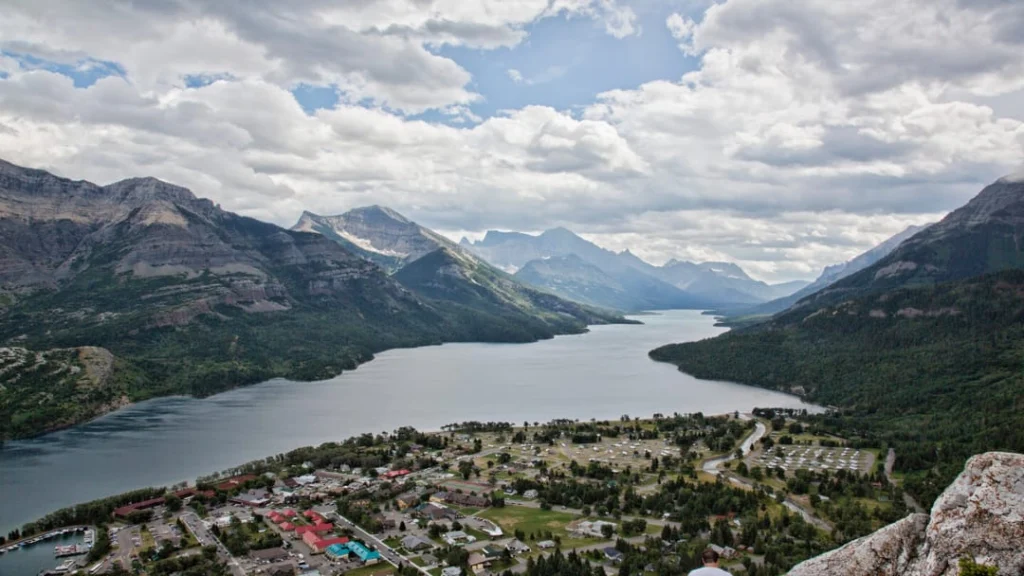 Panoramisch uitzicht over het dorp Waterton met een lang meer omringd door bergen onder een bewolkte lucht