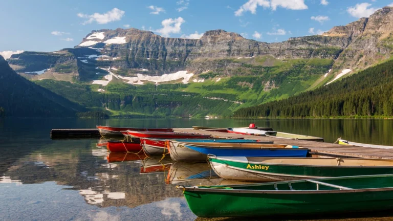 Rij kleurrijke kano's ligt afgemeerd aan een steiger op een spiegelglad meer in Waterton Lakes National Park, met besneeuwde bergen op de achtergrond