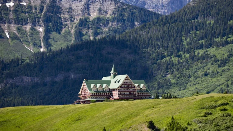 Het karakteristieke Prince of Wales Hotel met groen dak staat op een groene heuvel omringd door bebost berglandschap in Waterton Lakes National Park