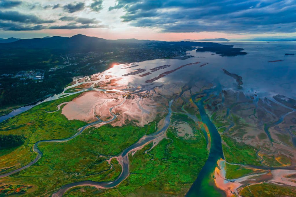 Luchtfoto van kronkelende rivierkanalen door groen moerasland dat uitmondt in zee, gekleurd door het licht van de zonsondergang