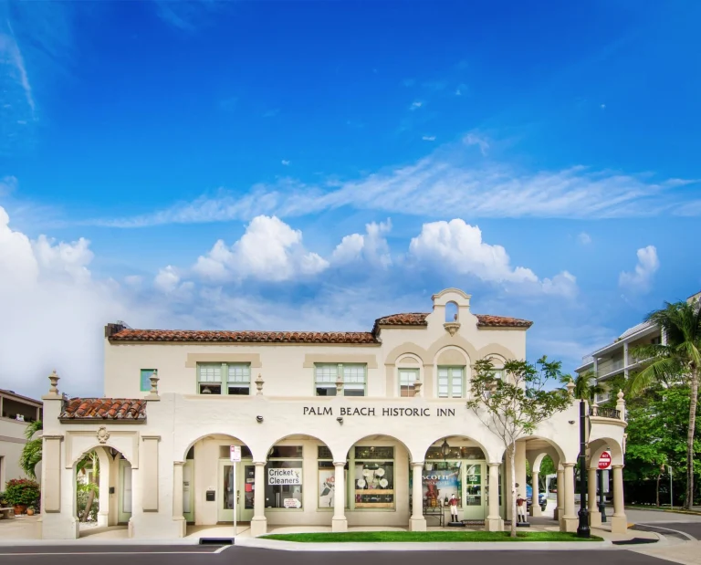 Wit koloniaal gebouw met rode dakpannen en booggangen van Palm Beach Historic Inn in West Palm Beach onder een zonnige hemel