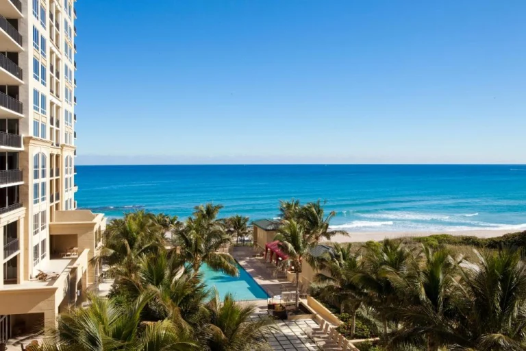 Uitzicht vanaf een hoog gelegen hotelbalkon in West Palm Beach op een zwembad omgeven door palmbomen met de oceaan op de achtergrond