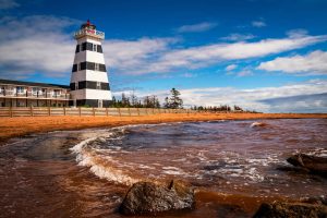 Zwartwit gestreepte vuurtoren naast een hotel aan het strand van West Point op Prince Edward Island bij golvend water